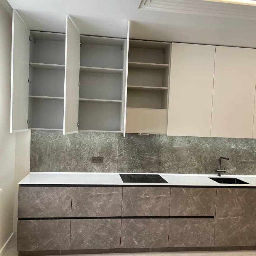 Широкая прямая кухня с высокими шкафами и фасадами под мрамор